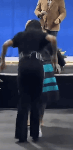 Man in Tan Jacket Behind Woman in Blue and Black Dress