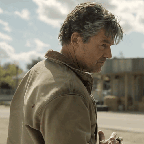 Man In Tan Jacket Standing In Front Of Building GIF