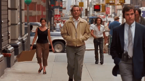 Man In Tan Jacket Walking Down Sidewalk GIF
