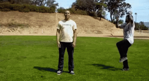 Man in Thrasher Shirt Jumping While Another Man Stands in Grass