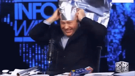 Man in Tin Foil Hat in Front of Info Wars Sign