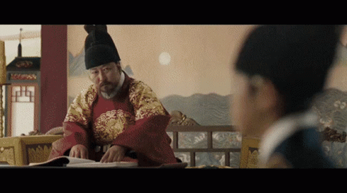 Man In Traditional Costume Reading Book, Another Looking On GIF