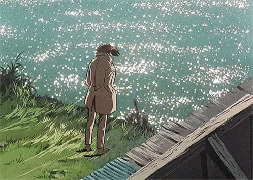 Man in Trench Coat Standing on Cliff Overlooking Ocean