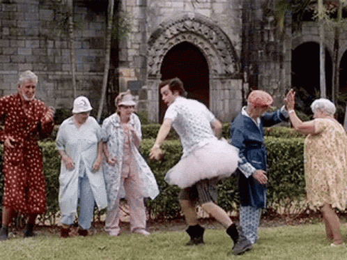 Man in Tutu Dancing With Elderly People in Front of Building