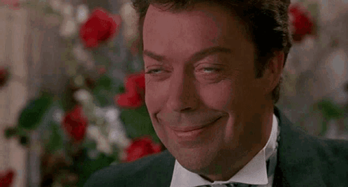 Man In Tuxedo And Bow Tie Smiling In Front Of Flowers GIF