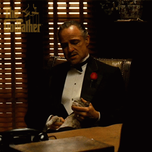 Man in Tuxedo at Desk With Blinds and Godfather Logo