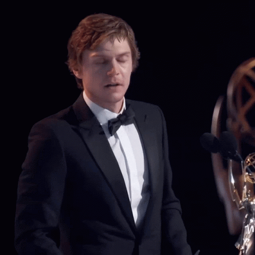 Man in Tuxedo Giving Speech at Two Microphones