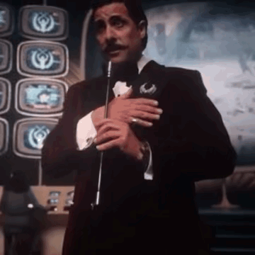 Man in Tuxedo Holding Microphone in Front of Televisions