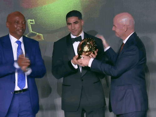Man in Tuxedo Holding Trophy Two Men Applaud