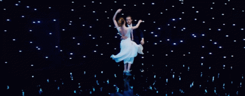 Man In Tuxedo Holding Woman In White Dress On Stage GIF