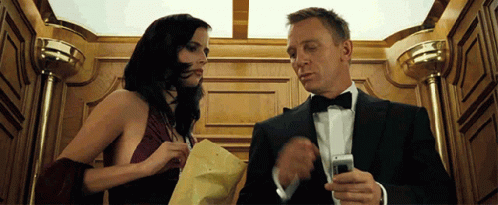 Man in Tuxedo Looking at Cell Phone Next to Woman