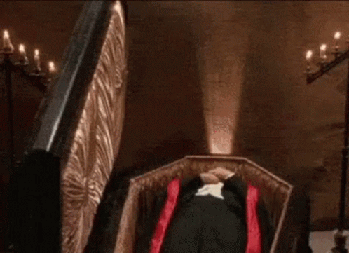 Man in Tuxedo Lying in Coffin with Red Cape