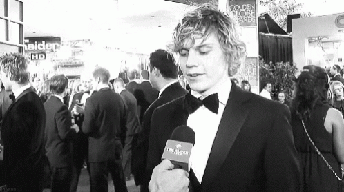 Man in Tuxedo Talking Into Microphone in Front of Crowd