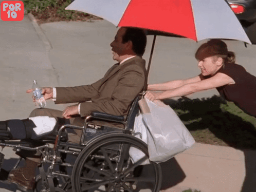 Man In Wheelchair Pushed By Woman Under Umbrella GIF