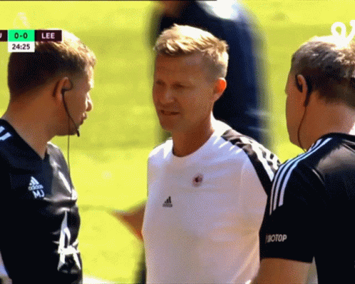 Man in White Adidas Shirt Talks to Two Men
