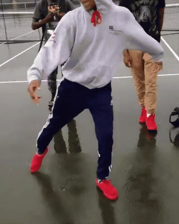 Man in White Hoodie and Blue Pants Dancing on Tennis Court