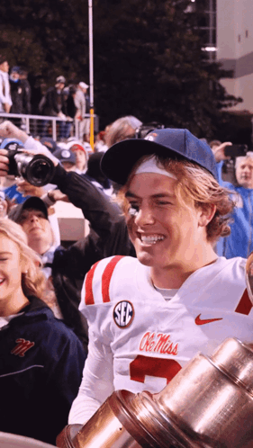 Man in White Ole Miss Jersey Holding Trophy