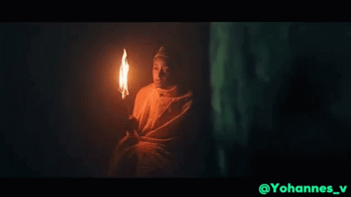 Man in White Robe Holding Torch in Dark