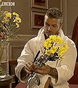 Man in White Robe Holding Yellow Flowers at BBC Sign