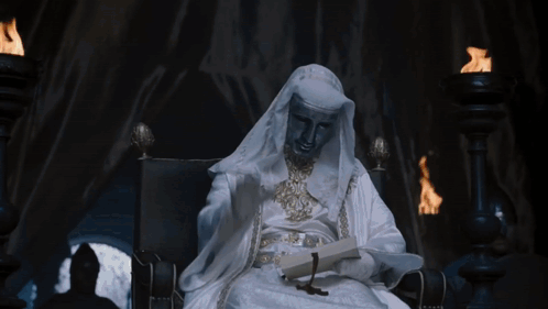 Man in White Robe Sitting in Chair Holding Book