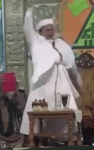Man In White Robe Speaking At Microphone GIF