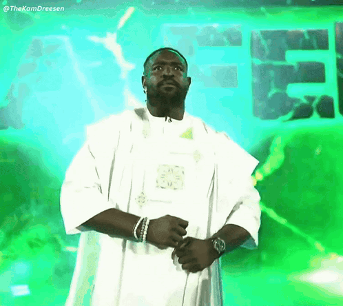 Man in White Robe Standing in Front of Green Sign Saying EE