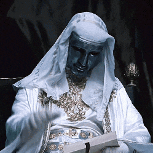 Man in White Robe with Blue Mask Reading Book