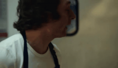Man in White Shirt and Apron in Front of Mirror