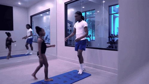 Man in White Shirt and Blue Shorts Jumping Over Blue Mat in Gym