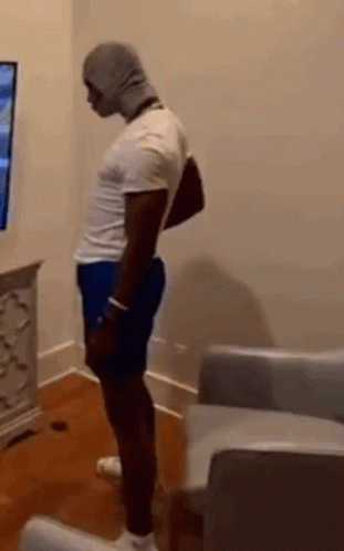 Man In White Shirt And Blue Shorts Standing In Front Of TV GIF
