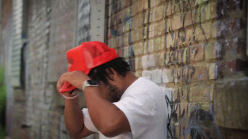 Man in White Shirt and Red Hat Leaning Against Brick Wall