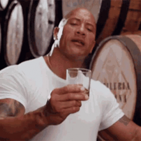 Man in White Shirt Holding Glass of Water in Front of Barrels