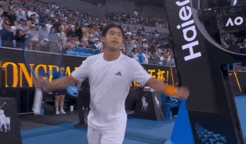 Man in White Shirt Holding Tennis Racquet in Front of Haier Banner