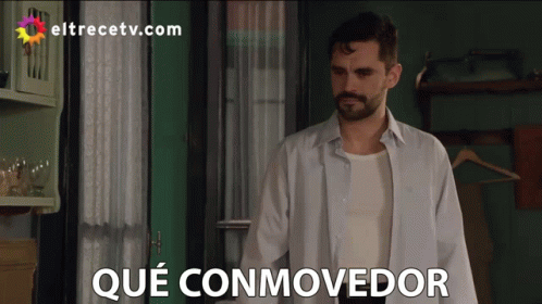 Man in White Shirt in Front of Que Conmovedor Sign