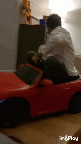 Man in White Shirt Riding Red Toy Car