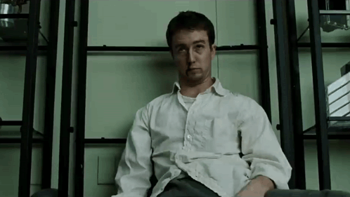 Man in White Shirt Sitting at Bookshelf
