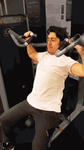 Man In White Shirt Using Gym Machine With Sign Saying Fitness GIF
