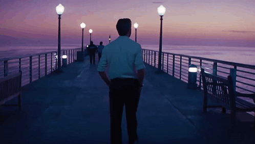 Man In White Shirt Walking Down Pier At Night GIF
