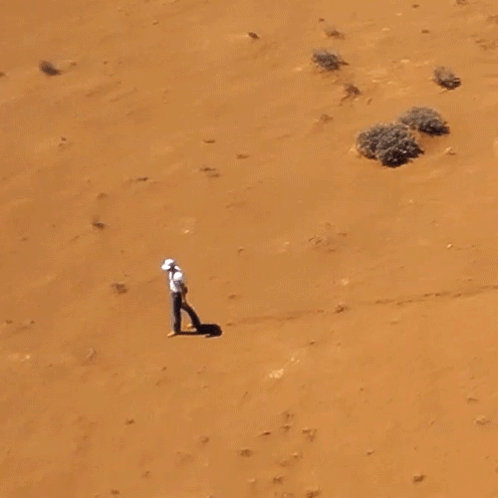 Man in White Shirt Walking in Sandy Desert