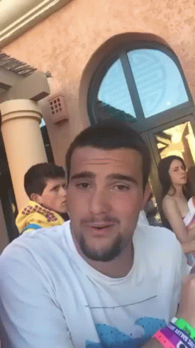 Man In White Shirt With Wave In Front Of Building GIF