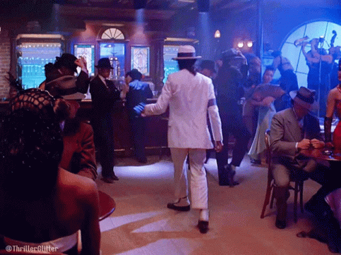 Man in White Suit Dancing in Room With People at Tables