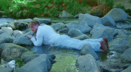 Man In White Suit Lying On Rocks GIF