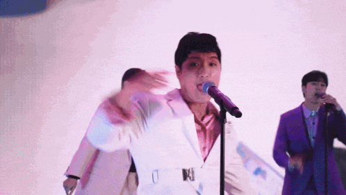 Man in White Suit Singing Into Microphone With Man in Purple Suit