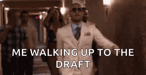 Man in White Suit Walking Up Hallway With People