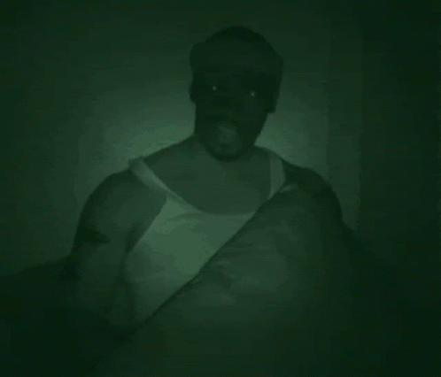 Man In White Tank Top Holding Pillow In Dark Room GIF