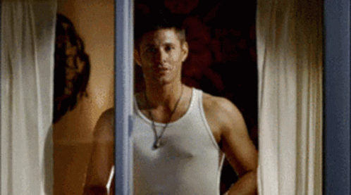 Man In White Tank Top Looking Out Window GIF