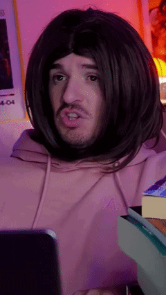 Man in Wig and Pink Hoodie Looking at Cell Phone