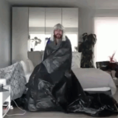 Man in Wig Wrapped in Black Bag in Living Room