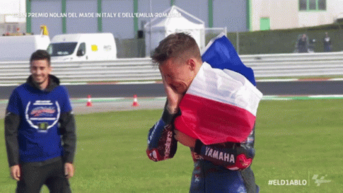 Man In Yamaha Jacket Holding French Flag Over Head GIF