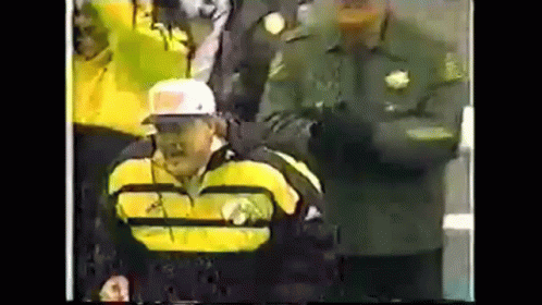Man in Yellow Jacket and White Hat in Wheelchair in Front of Crowd
